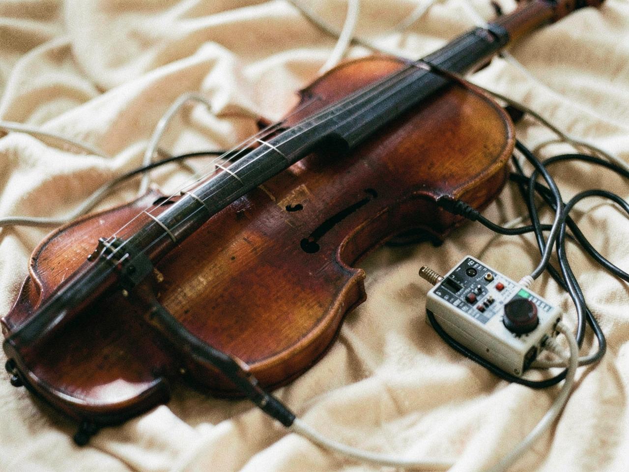 A violin resting beside audio cables and a small interface on warm linen